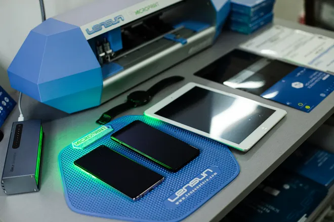 Máquina de corte de películas Lensun com telemóveis e um tablet na bancada