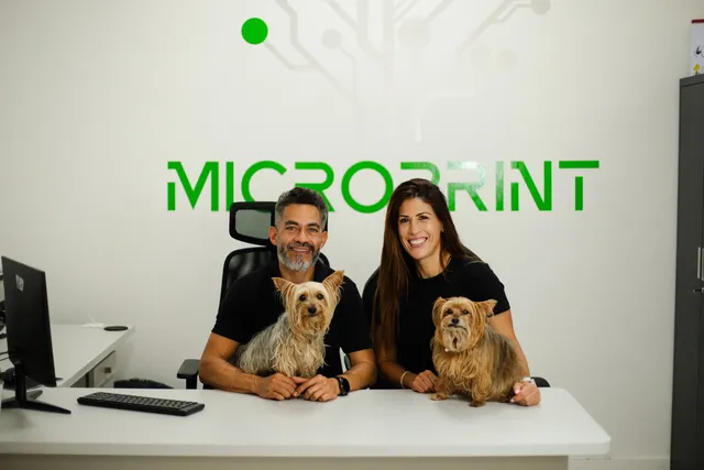 Dois membros da equipa à secretária com dois cães, com o logótipo Microprint na parede