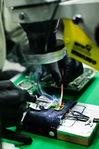 Técnico de luvas a soldar componentes numa placa eletrónica