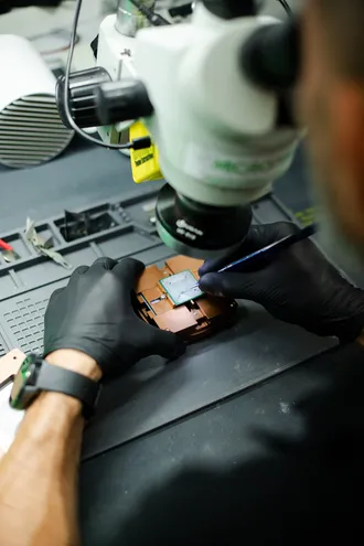 Técnico a trabalhar ao microscópio numa placa eletrónica